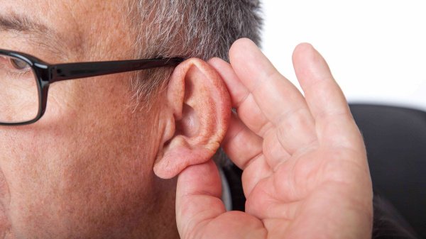 Mann streckt das Ohr nach vorne mit einer Hand, um besser hören zu können.