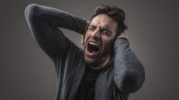 Ein Mann leidet an Anpassungsstörung und hält sich vor lauter Lärm die Ohren zu, während er schreit, da es kaum erträglich ist.