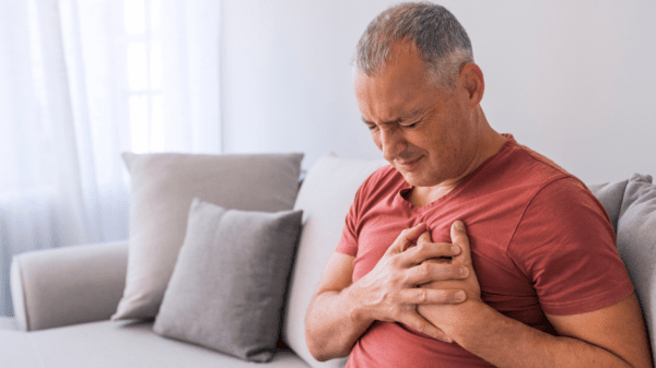 Ein Mann mit Brustschmerzen sitzt auf dem Sofa fasst sich mit einem Schmerzgesicht an die Brust.