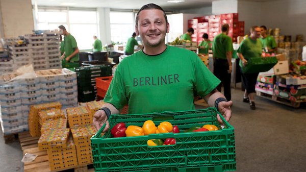 Mann mit der Berliner Tafel mit einem Korb voller Gemüse in der Hand.