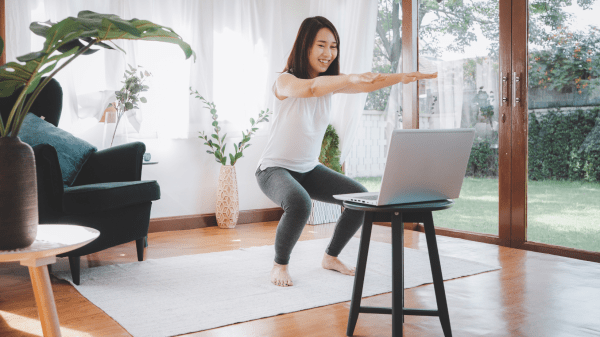 Eine Frau bei einer Sportübung zuhause vor dem Laptop