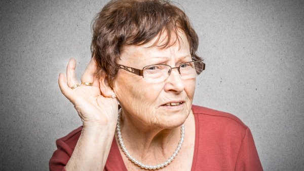 Frau hält sich die Hand ans Ohr um zu signalisieren, dass sie schwer hören kann.