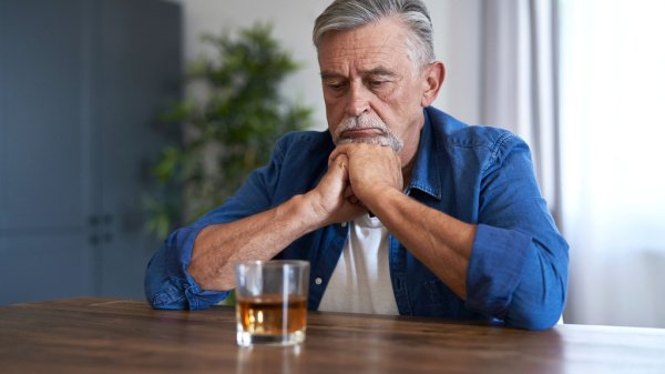 Ein nachdenklicher Mann sitzt mit gefalteten Händen vor einem Glas Alkohol, das symbolisch für seine Alkoholsucht steht.