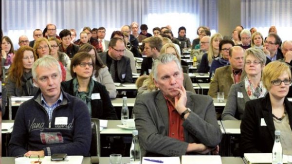 Mehrere Menschen sitzen in einem Raum und hören aufmerksam zu