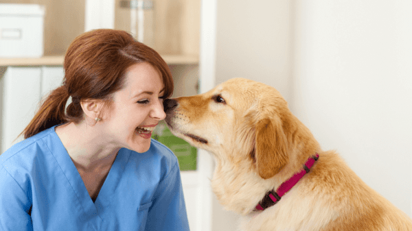 Pflegefachkraft sitzt neben einem Hund und lacht vor Freude.