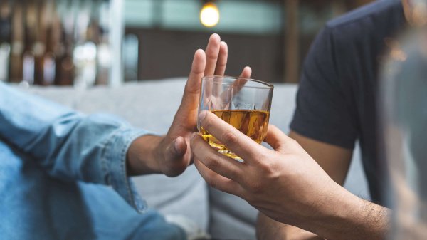 Person gibt anderer Person ein Glas mit Alkohol, welche mit Geste ablehnt.