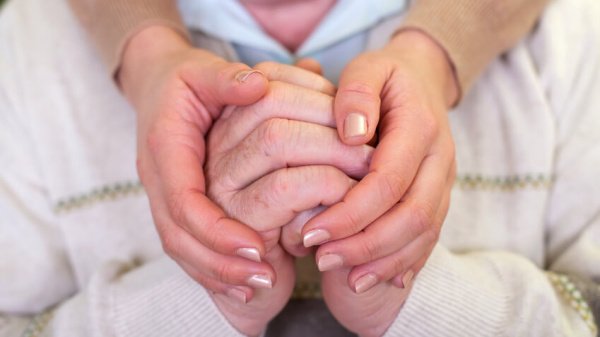 Ein Patient bekommt emotionalen Beistand, symbolisiert durch die Berührung der zusammengefalteten Hände durch eine andere Person.