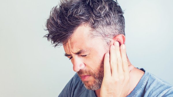 Mann hält sich das linke Ohr mit seiner Hand aufgrund eines Tinnituses.