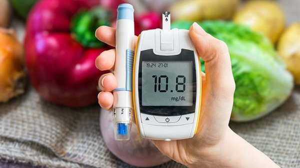 Blutzuckermessgerät, Insulinpen vor Gemüse gehalten von einer Hand.