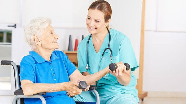 Pflegende kümmert sich um geriatrische Patientin im Rollstuhl