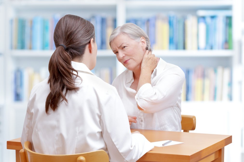 Gespräch zwischen Ärztin und Patientin, die sich den Nacken vor Schmerzen hält.