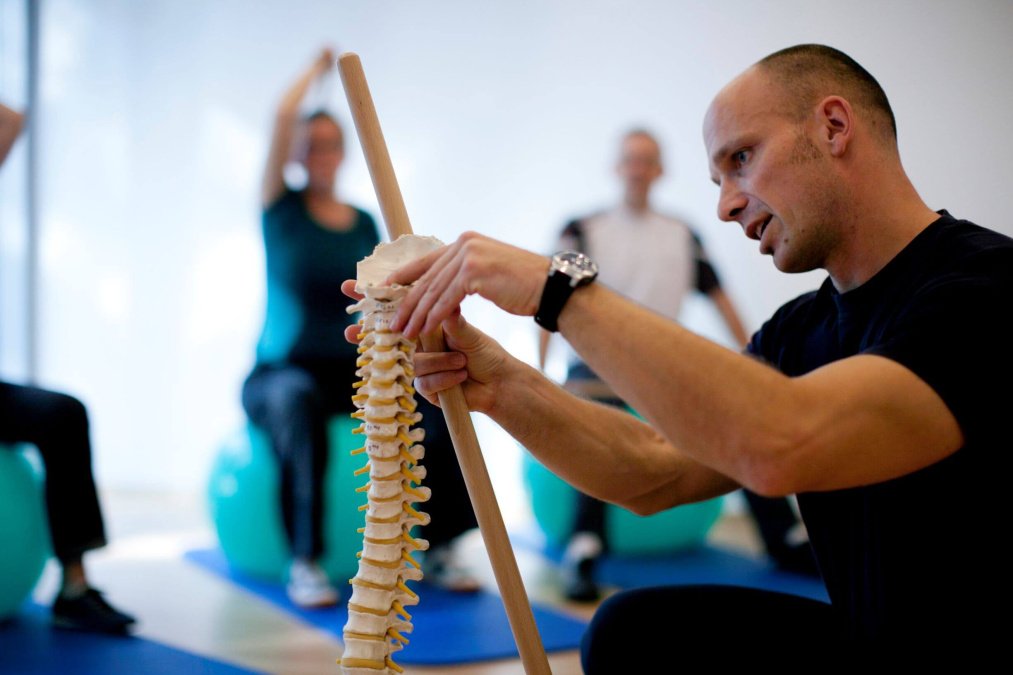 Physiotherapeut erklärt anhand eines Wirbelsäulen-Modells das Ziel der Übungen. 