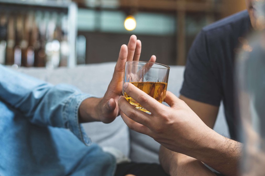 Person gibt anderer Person ein Glas mit Alkohol, welche mit Geste ablehnt.
